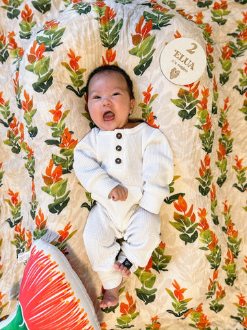 napua - 2 months old in white kahi romper. laying on a liko lehua bamboo swaddle next to an ohia lehua pillow