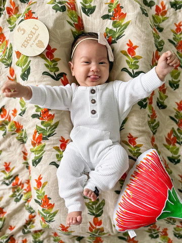 napua - 3 months old in white kahi romper. laying on a liko lehua bamboo swaddle next to an ohia lehua pillow