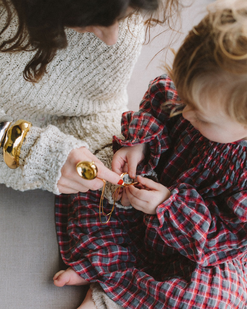 A woman is helping a little girl put on a misho designs necklace.