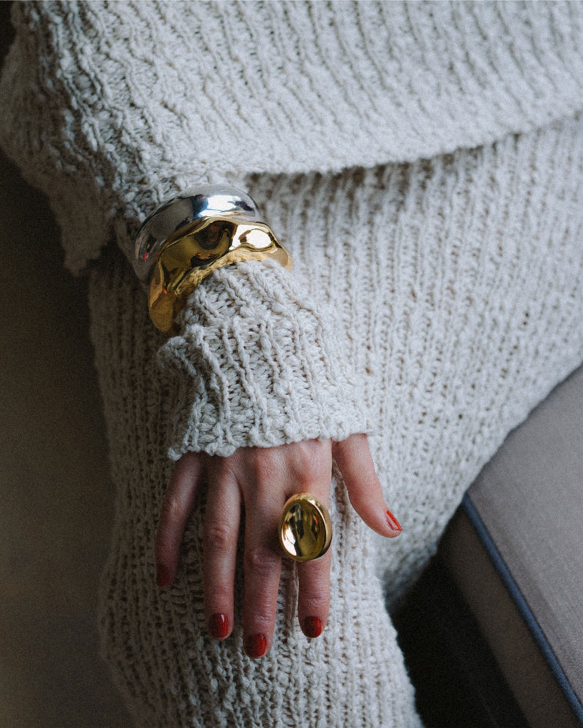 A woman sitting on a couch with a gold misho designs ring on her finger.
