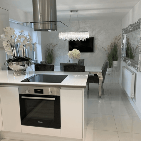 A high gloss white kitchen looks out over the dining area, which features a stunning ornate silver framed mirror and a glass chandelier