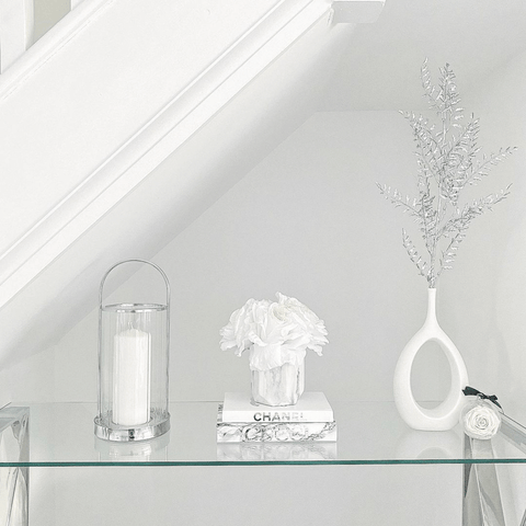 Delicate ornaments and vases decorate a glass topped console table under the stairs.