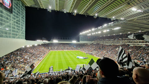 A packed St. James' Park during a Newcastle United football match, with cheering fans in the stands
