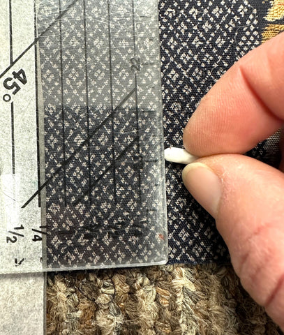 Clear ruler on a dark fabric and fingers with chalk marking a line.