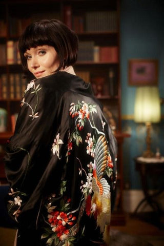 Phryne Fisher wearing a black embroidered silk kimono.  Her back is to the camera and she's looking over her left shoulder.