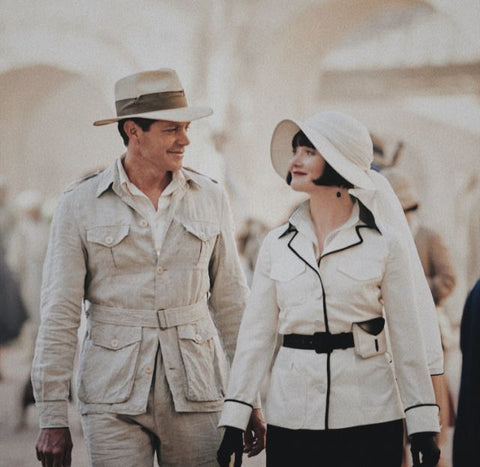 Man and woman dressed in safari clothes from the 1920s walking in a street, looking at each other
