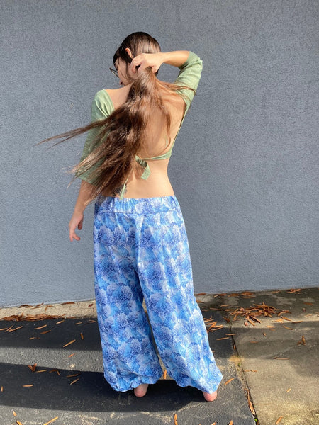barefoot woman with long brown hair standing in front of grey wall with green crop choli top and blue print pantaloons. - back to to viewer