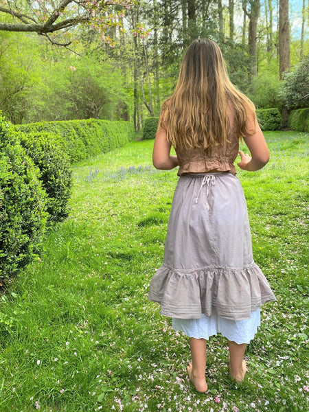 Back of woman wearing a purple petticoat, outside by a hedge.