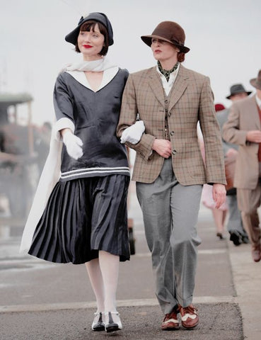 Two women walking along a road, one waring a maritime middie and skirt and the other wearing a mans suit.