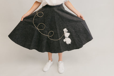 Grey poodle skirt with a white poodle embroidered on it.  Photo of girl from waist down.
