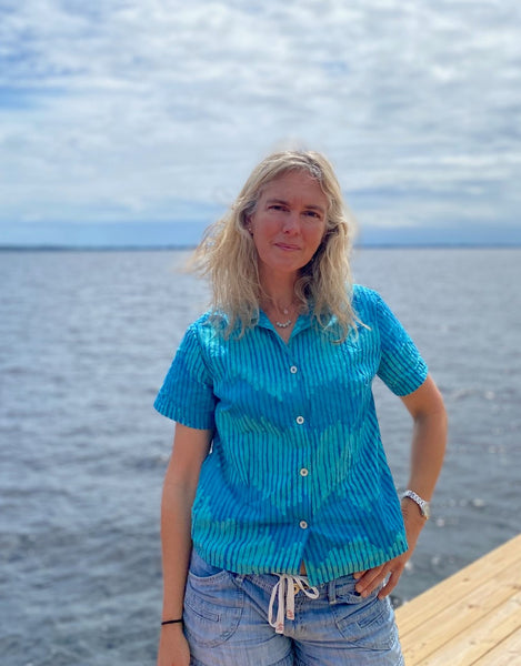 Woman standing by a river wearing a teal block printed button down shirt.