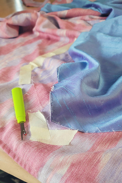 Adjusting the 261 Paris Promenade Dress of pink fabric with blue overlay with a seam ripper and tape.