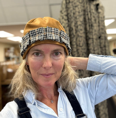 Woman in a brown hat with a black and white band and a blue shirt. Her hand is by her head