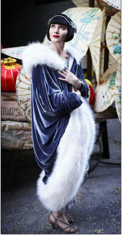 Miss Fisher wearing a blue velvet cocoon coat trimmed with white fur.
