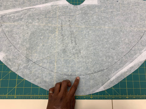 Pattern skirt piece cut out of tracing paper, on green cutting mat. African American hand pointing to indicate which view to cut for on the skirt piece.