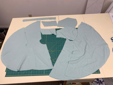Pattern pieces cut out of aqua light blue fabric on a green cutting mat.