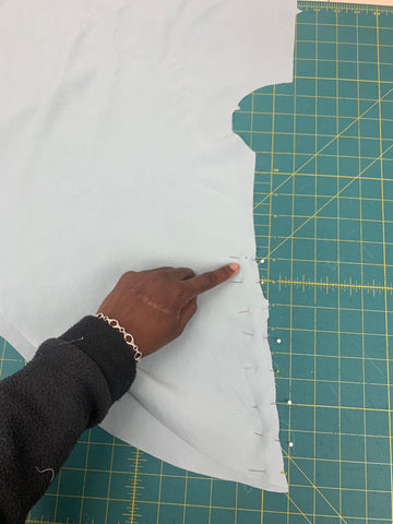 Pinned Center Back Seam  Skirt Back F from dot to hem on a green cutting mat. African American hand pointing to the dot.