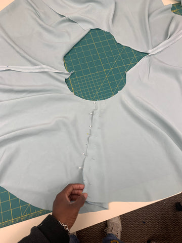 Pinned Skirt Front E to Skirt Back F at side seam on a green cutting mat, held with an African American hand at the bottom hem
