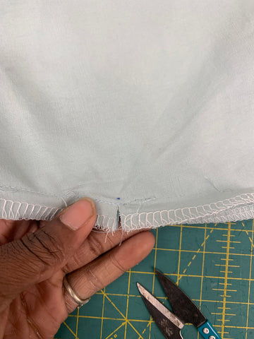 Close up of clipping to dot on Skirt back F, held by an African American hand with sewing scissors on a green cutting mat.