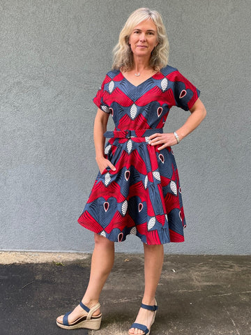 woman standing in front a grey wall wearing a knee length blue and red fit and flair dress.  Left hand is on hip.