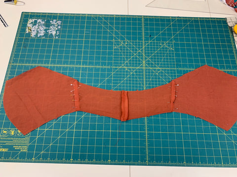 Right sides together, pinned orange fabric back B to FRONT BODICE A at side seams, matching notches. Laid out on a green cutting mat.