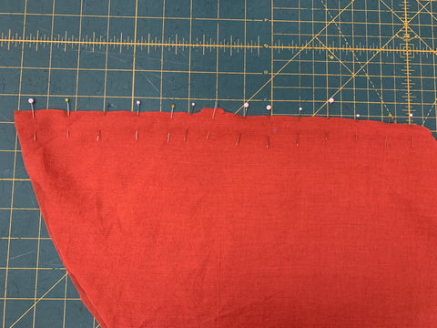Right sides together, pinned center back seam on orange fabric BACK SKIRT F matching notches on a green cutting matt.