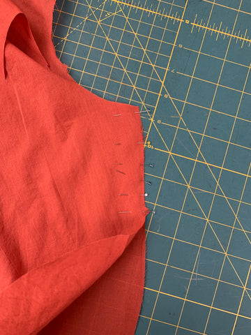Close up of right sides together, pinned orange FRONT SKIRT E to BACK SKIRT F at side seams stopping at single notches on a green cutting mat.