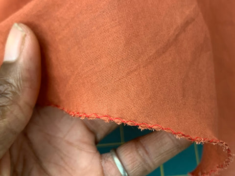 Close up of zig-zaged hem on orange hem of skirt help with an african american hand.
