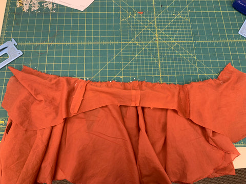 Right sides together, pinned orange skirt to bodice laid out on a green cutting mat.
