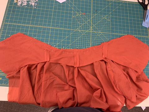 Pinned orange lining to the orange bodice at neckline right sides together, skirt is attached to outer layer  of bodice, laid out on a green cutting mat.