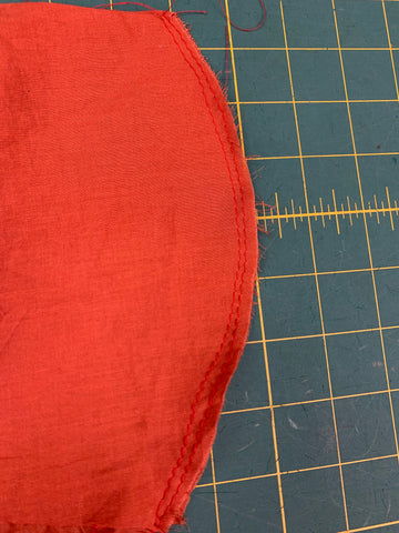 Close up of gathering stitches placed ⅛” (3mm) from left center orange front bodice A on a green cutting mat.