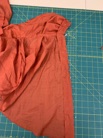 Pinned pressed open side of orange bias binding to wrong side of left orange garment front on a green cutting mat.
