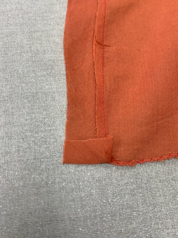 Close up of folded under 1/2"(13mm) at  bottom edge of orange bias binding to center front on a light grey background.