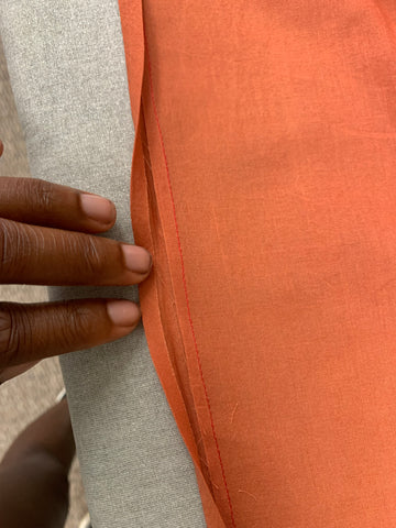 Close up of african american hand  turning orange bias binding to right side over remaining seam allowance on a grey background.