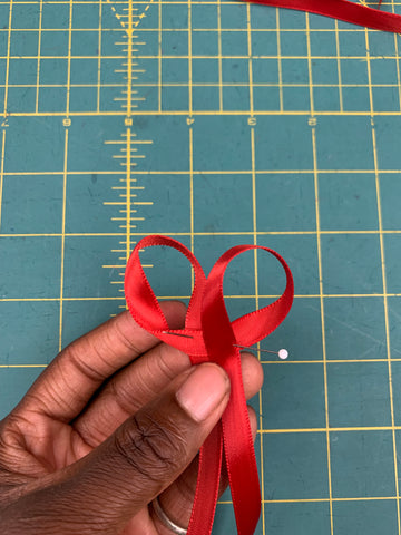 Two loops pinned together in the center held by an African American hand on a green cutting mat.