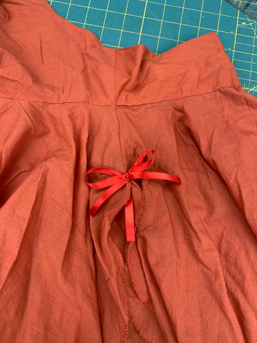 Red ribbon bow sewn on side seam of orange garment