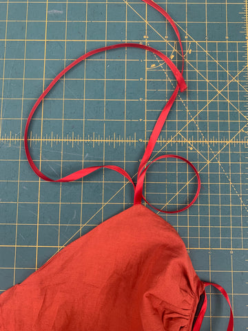 Two red ribbons stitched to orange bodice front on a green cutting mat.