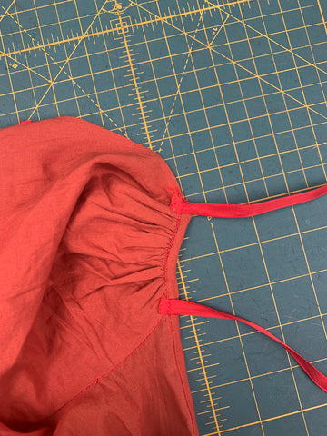 Red ribbons sewn to inside of center front gathered bodice, on a green cutting mat