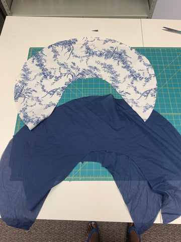 Three pieces of the curved collar D, on the top is cut out of the outer fabric blue and white french toile and two below are cut out from the navy cotton voile, all laying out on a green cutting mat.