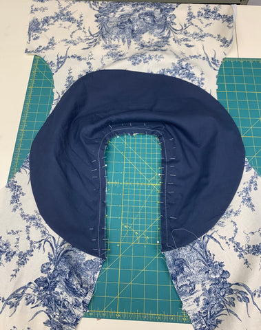 Navy Blue collar D pinned to outside of the assembled front and back pieces cut out of french toile canvas fabric, on a green cutting mat.