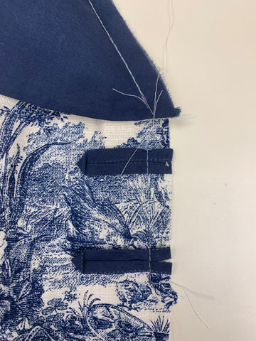 Close up of navy blue button loops basted to the french toile fabric bodice front opening, on a white background.