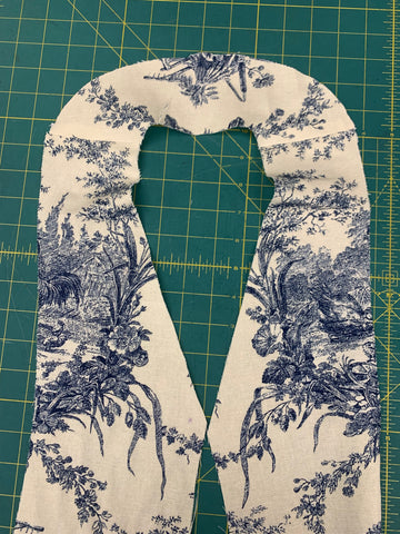 right side facing up showing blue and white french toile fabric of neck and front facings attached at shoulder seam, laying on a green cutting mat.