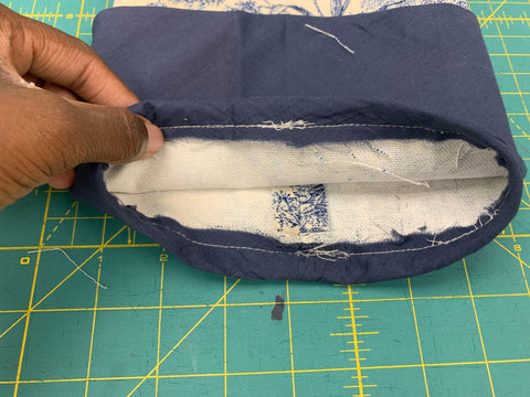 African American Hand holding cuff attached to sleeve open to see the inside of the turn up the Cuff 1/2” (1.25cm) from seam so that seam is tucked up inside Sleeve, on a green cutting mat.