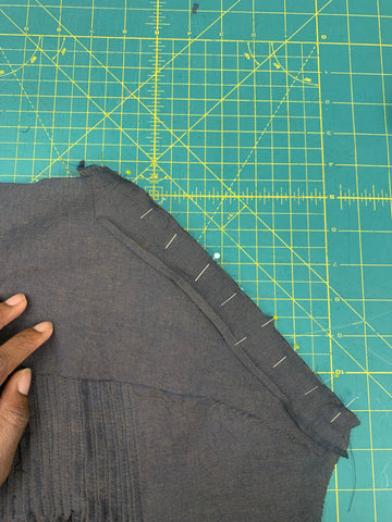 Pinned facing J to the wrong side of sleeve C with a hand placed on the garment, on a green cutting mat.