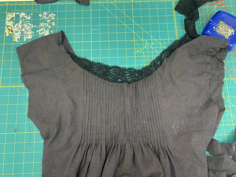 Black lace placed on neckline of pleated bodice front on a green cutting mat.