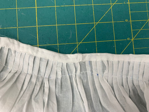 Bias binding topstiched down to the inside of the bodice neckline out of a cotton voile in white.