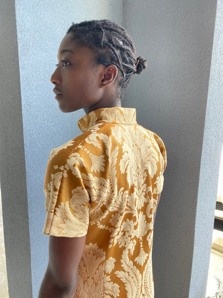 Woman, standing with back toward camera, in a gold brocade Cheongsam