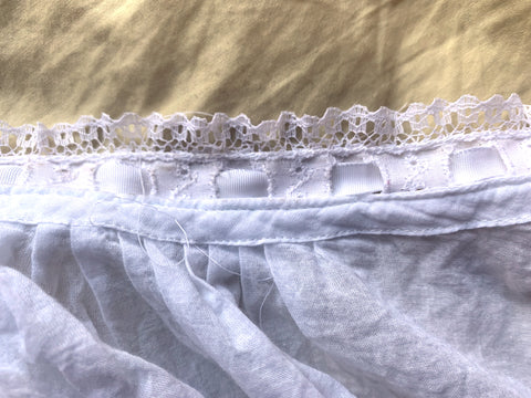close up of the wrong side of white eyelet ruffle with a white ribbon through the eyelet stitched on the neckline of the garment.
