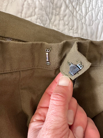 close up of a hook and eye on the back of a khaki green pair of pants.