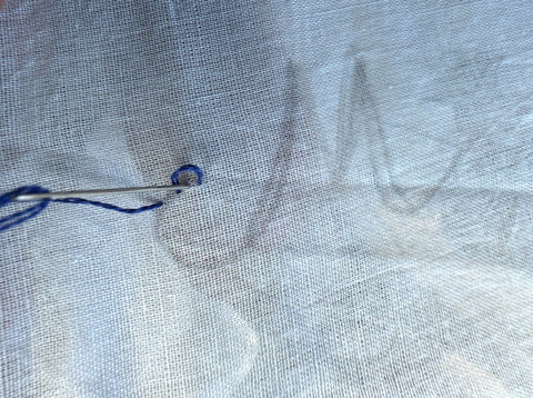 Letter M on white fabric, beginning embroidery with blue thread.